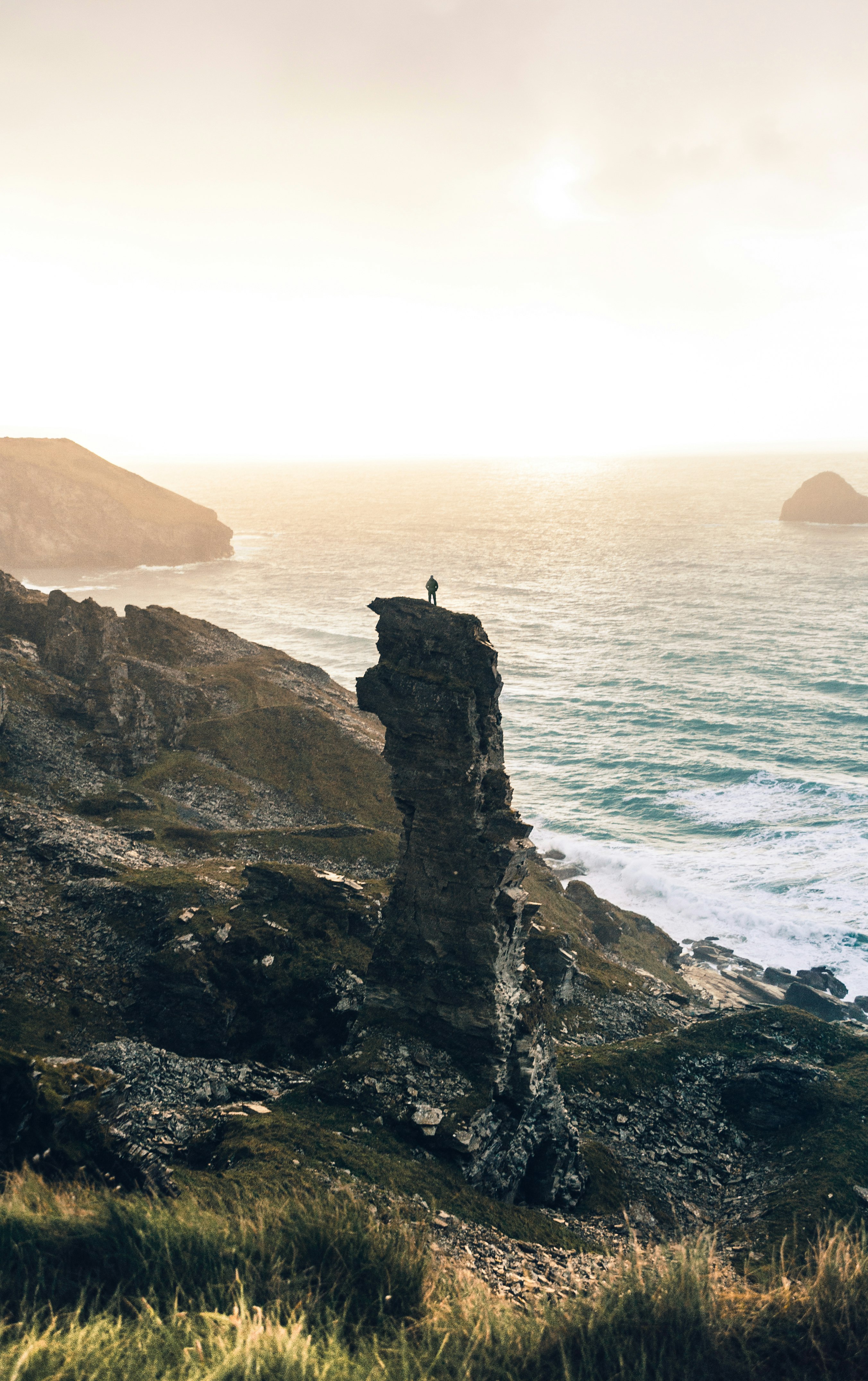 man standing on rock cliff near body of water